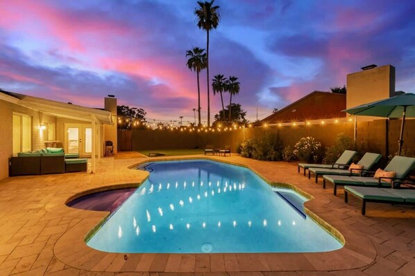 A swimming pool with water jets, lounge chairs, and a sunset sky.
