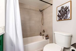 A bathroom with a bathtub, toilet, shower, and a framed artwork on the wall.