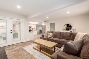 A modern living room with a sofa, coffee table, and a kitchen in the background. - Obispo Modern Oasis with Heated Pool and BBQ (Mesa)