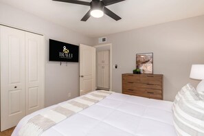 A bedroom with a bed, a wooden dresser, a television, and a ceiling fan.