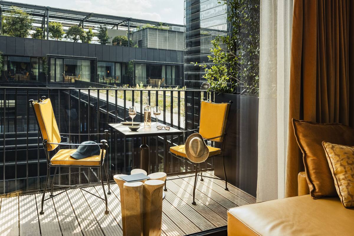 A balcony with yellow chairs, a table with glasses, and a view of buildings.