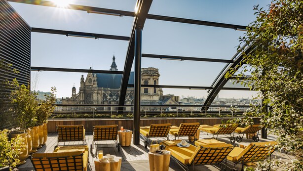 A rooftop terrace with yellow seating, potted plants, and a view of historic buildings. - Hôtel Madame Rêve (Paris)