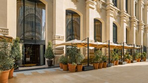 A hotel exterior with large arched windows, outdoor seating with umbrellas, and potted plants. - Hôtel Madame Rêve (Paris)