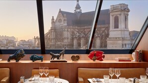 A restaurant with tables set for dining, a view of a historic building, and decorative animal figurines on the counter. - Hôtel Madame Rêve (Paris)