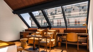 A cozy loft bedroom with a large skylight, a wooden desk, a comfortable sofa, and a small round table. - Hôtel Madame Rêve (Paris)