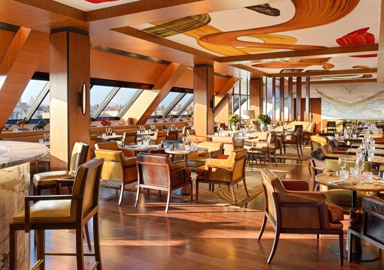 A spacious restaurant with high ceilings, modern wooden paneling, and large windows offering city views.