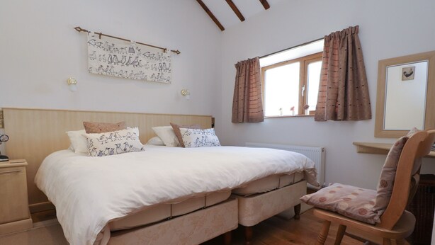 A bedroom with a double bed, a wooden nightstand, a chair, a window with curtains, and a wall-mounted artwork. - The Proven House (Preston)