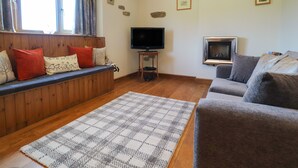 A living room with a wooden bench, a grey sofa, a television, and a fireplace. - The Proven House (Preston)