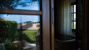 A view through a window of a garden with a stone wall, a fountain, and a building with two tall structures in the background. - Le Rose di Montagnana (San Gimignano)