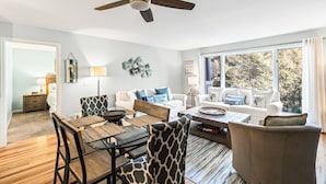 A modern living room with a dining area, large windows, and a ceiling fan. - Lagoon Villa 19 - Lagoon Lifestyle! Center Resort! (Isle of Palms)