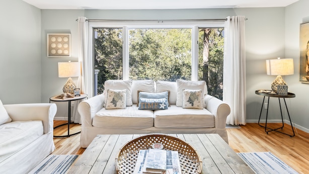 A living room with a sofa set, a coffee table, and a view through large windows. - Lagoon Villa 19 - Lagoon Lifestyle! Center Resort! (Isle of Palms)