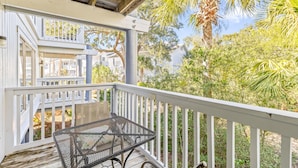 A wooden deck with a metal table and chairs, overlooking a residential area with houses and palm trees. - Lagoon Villa 19 - Lagoon Lifestyle! Center Resort! (Isle of Palms)