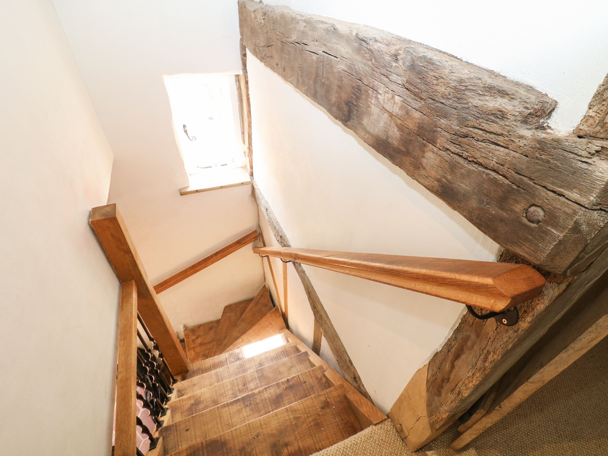 A wooden staircase with a rustic finish, leading to a landing with a small window.