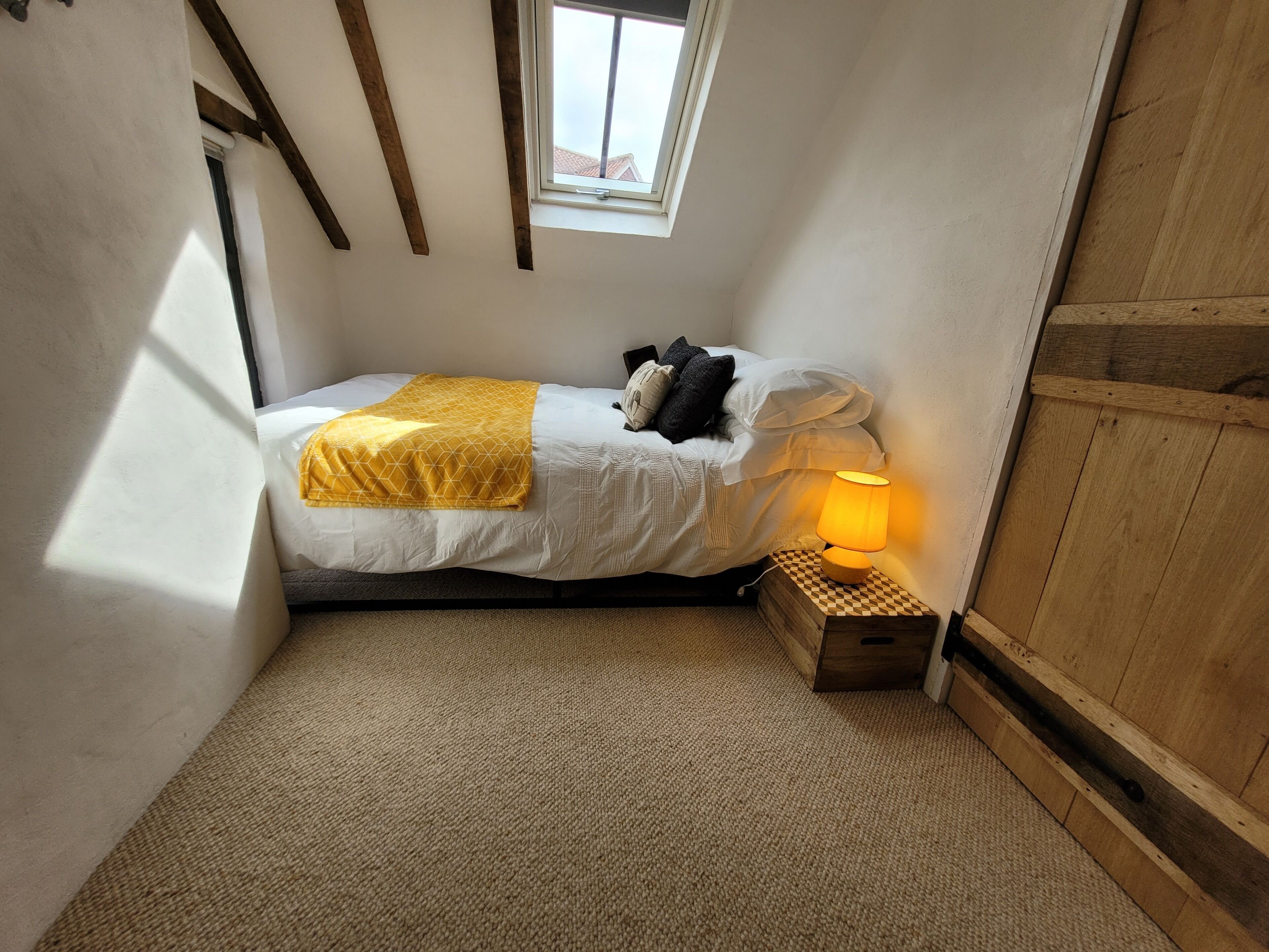 A small, cozy bedroom with a bed, a bedside lamp, and a window.