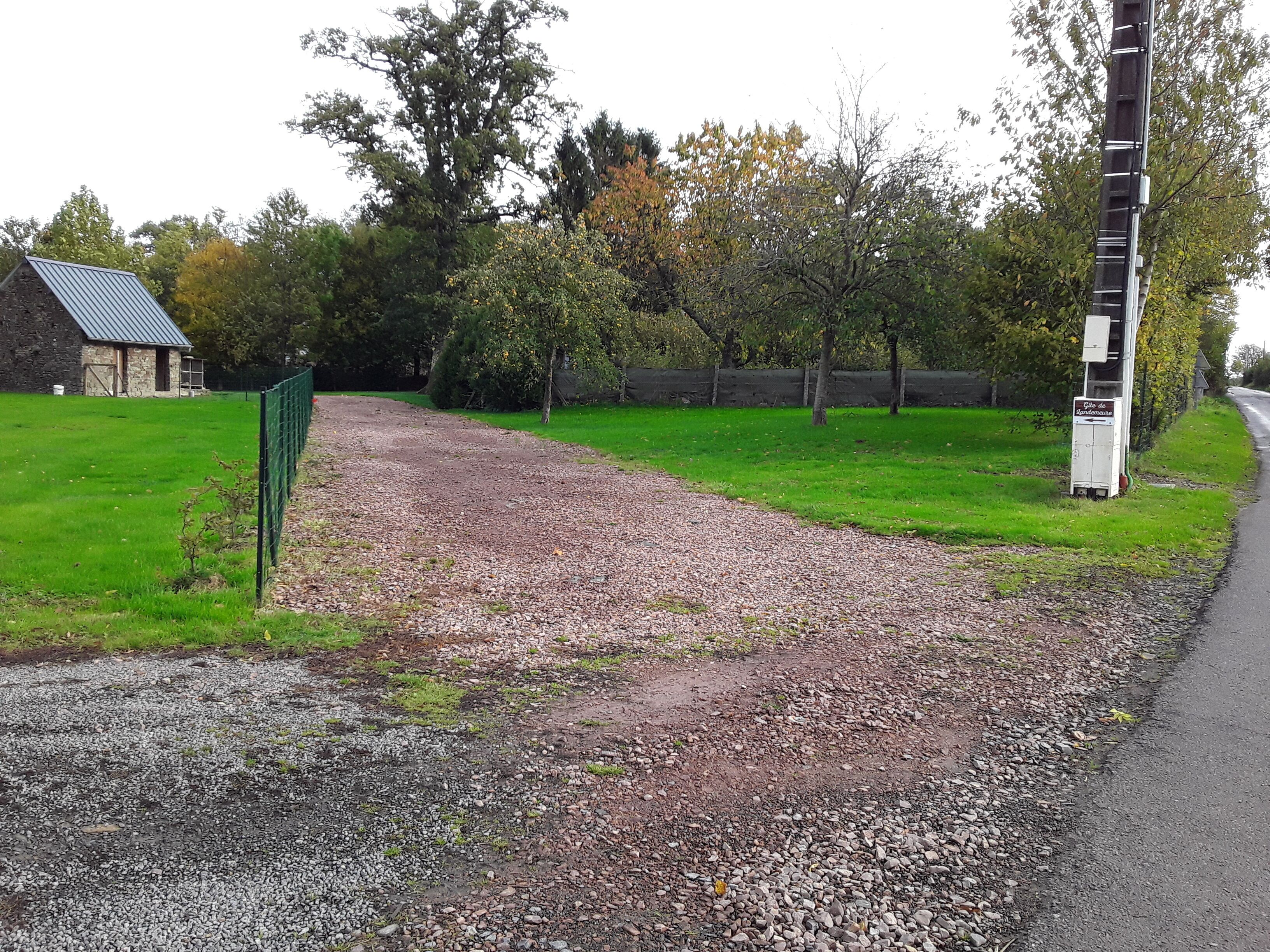 A gravel path leading to a stone building with a metal roof, surrounded by green grass and trees.