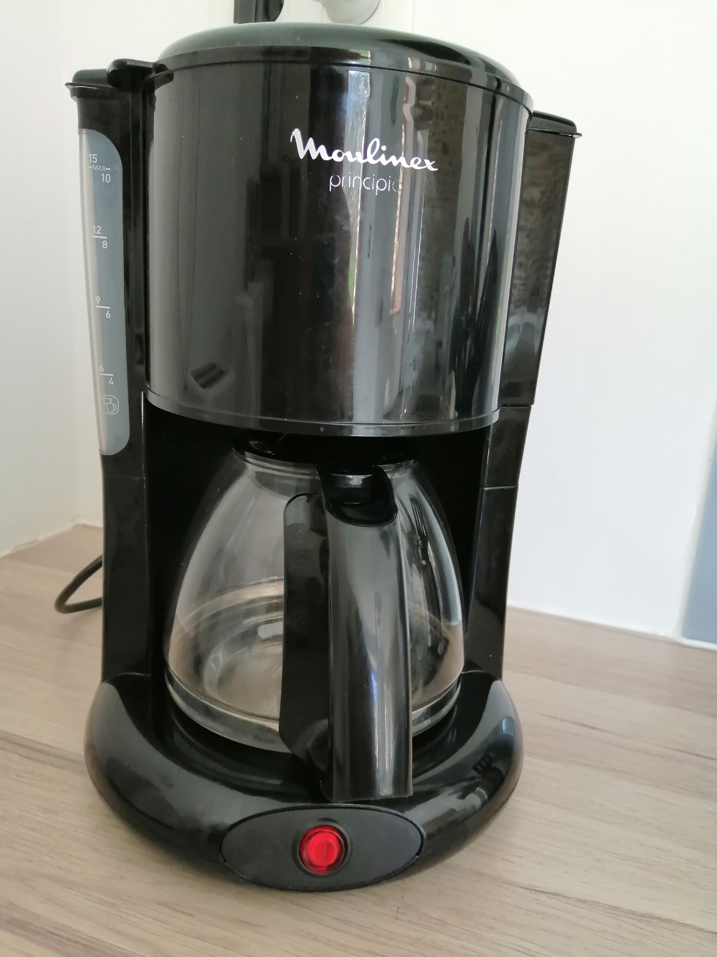A black coffee maker with a clear water reservoir and a red power button.