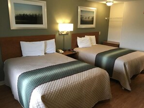 Habitación de hotel con dos camas, una mesita de noche con lámpara y cuadros en la pared.