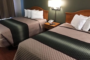 Habitación de hotel con dos camas, cada una con colcha acolchada, cabecero de madera, mesita de noche con teléfono y control remoto, y una lámpara de pared.