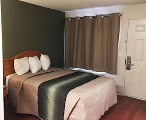 Una habitación de hotel con cama, puerta y ventana con cortinas.