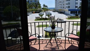 A balcony with a round table and two chairs, overlooking a parking lot with several cars and a building with balconies. - Oceans 735 (Deerfield Beach)