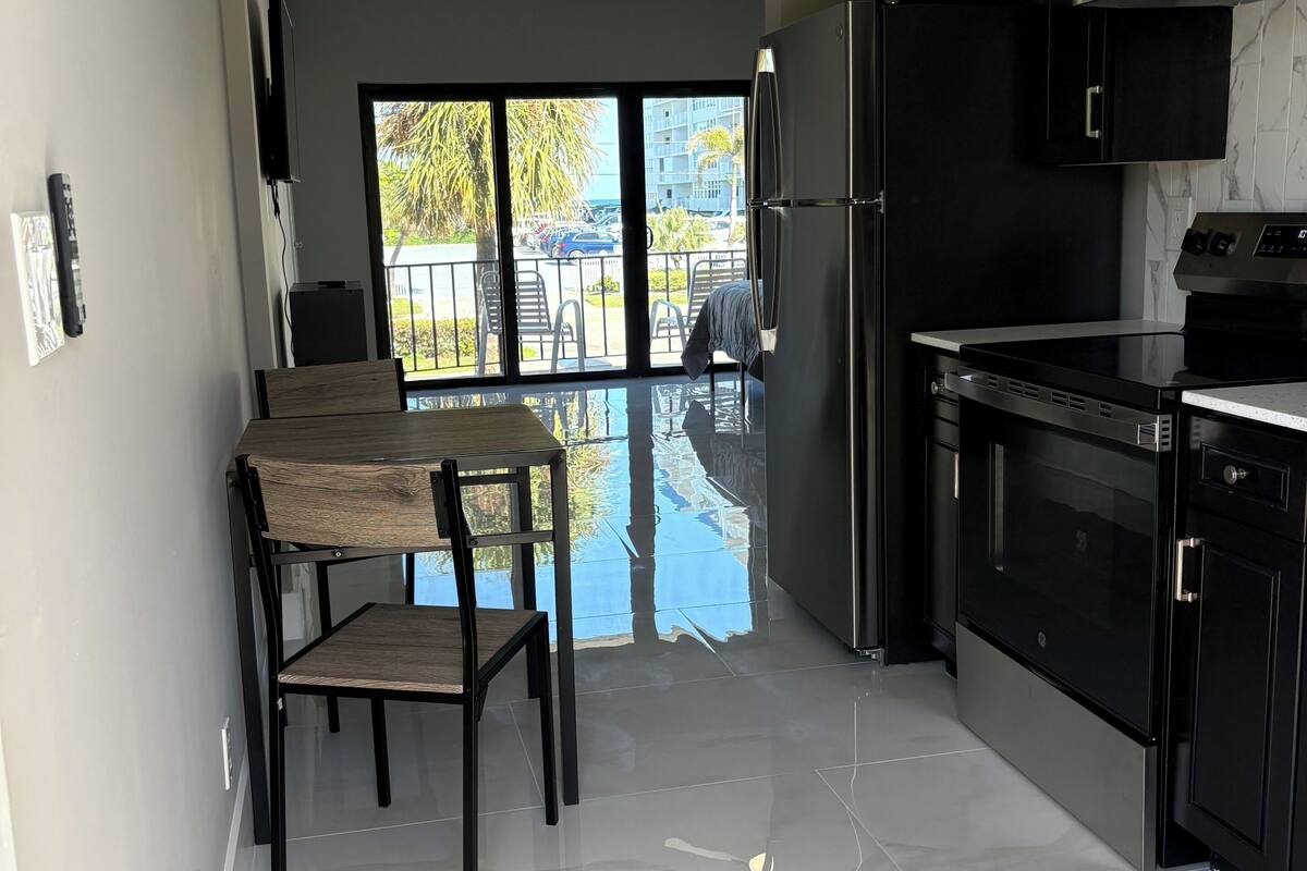 A modern kitchen with a dining area, large windows, and a view of the outdoors.