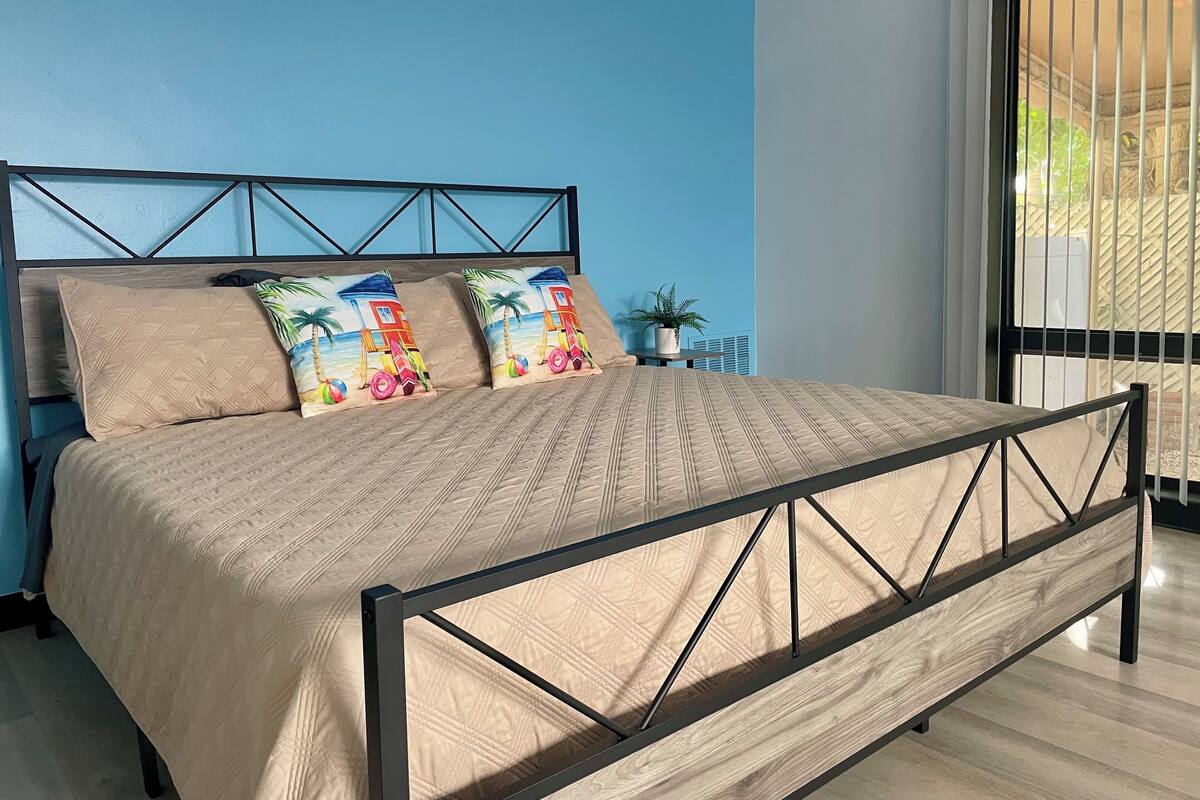 A bed with a metal frame, beige bedding, and two colorful pillows.