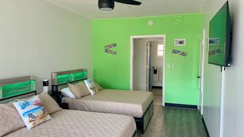 Une chambre avec deux lits, un ventilateur de plafond, une télévision et un mur peint en vert.
