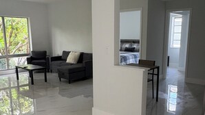 A spacious living room with a ceiling fan, a sofa, a coffee table, and a view of a bedroom through an open doorway. - Oceans 735 (Deerfield Beach)