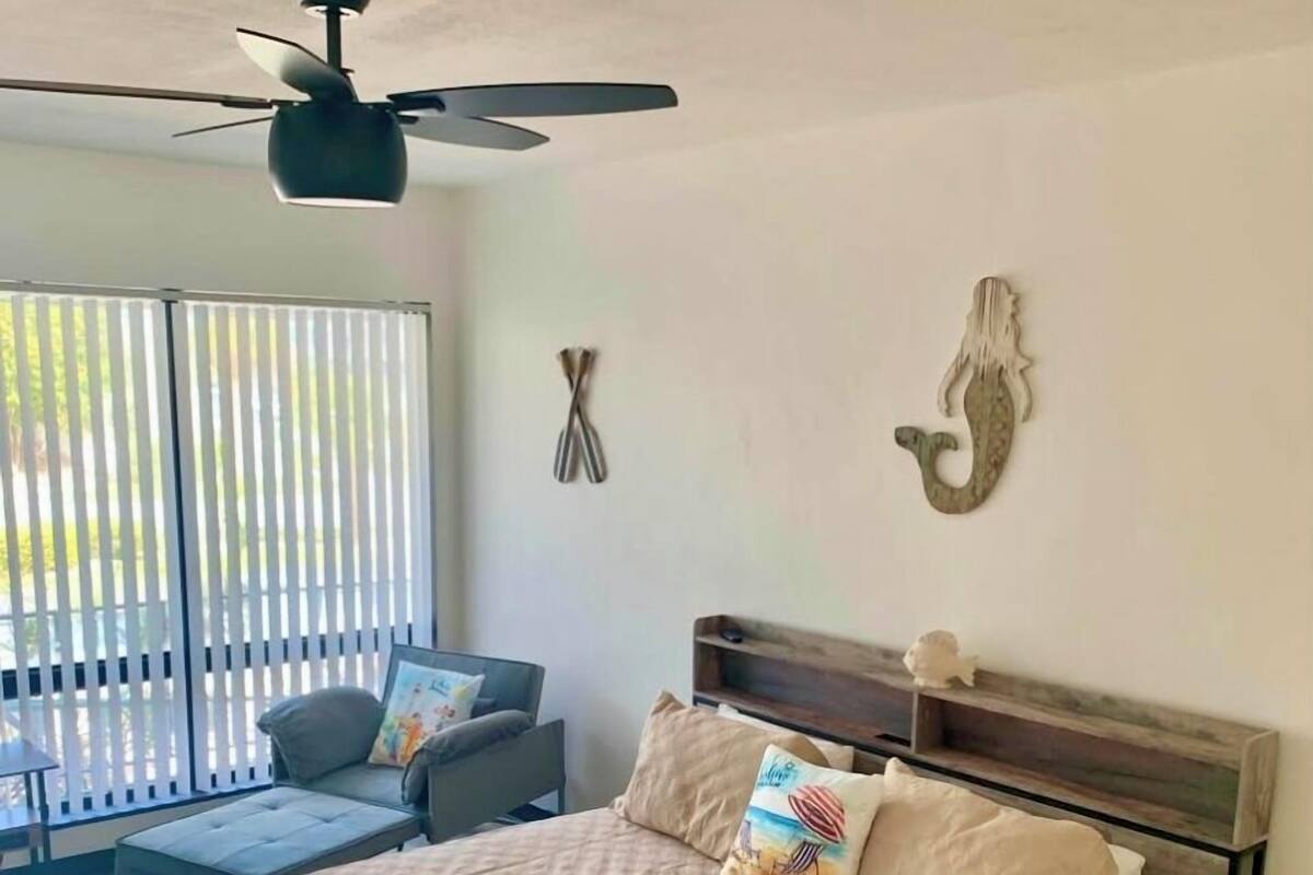 A bedroom with a bed, a ceiling fan, a sofa, and a view through the window.