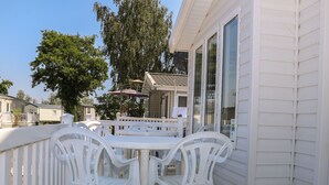 A white deck with a table and chairs, overlooking a residential area with houses and trees. - The Goodwood Lodge (Chichester)
