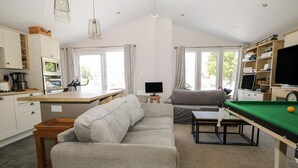 A modern living space with a sofa, a pool table, a television, and a kitchen area. - The Goodwood Lodge (Chichester)