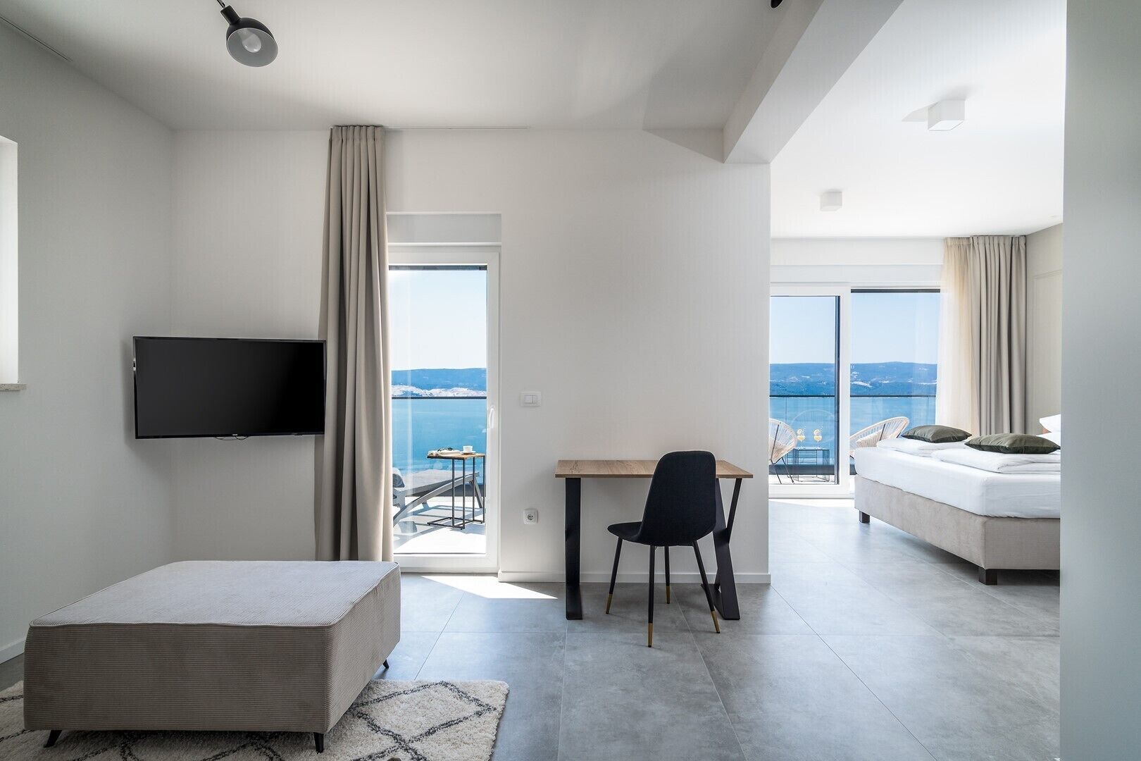 Une chambre d’hôtel moderne dotée d’une télévision à écran plat, d’un coin repas avec une table et des chaises, d’un canapé et d’un balcon offrant une vue sur la mer.