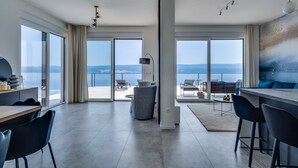 A modern hotel room with a large sliding glass door leading to a balcony with a view of the sea. There is a dining area with a table and chairs, and a seating area with a sofa and a coffee table. - Seaview Villa Marila with a private heated pool with hydromassage, 3 en-suite bedrooms (6+2 people), 1km from the beach (Lokva Rogoznica ( Omis))