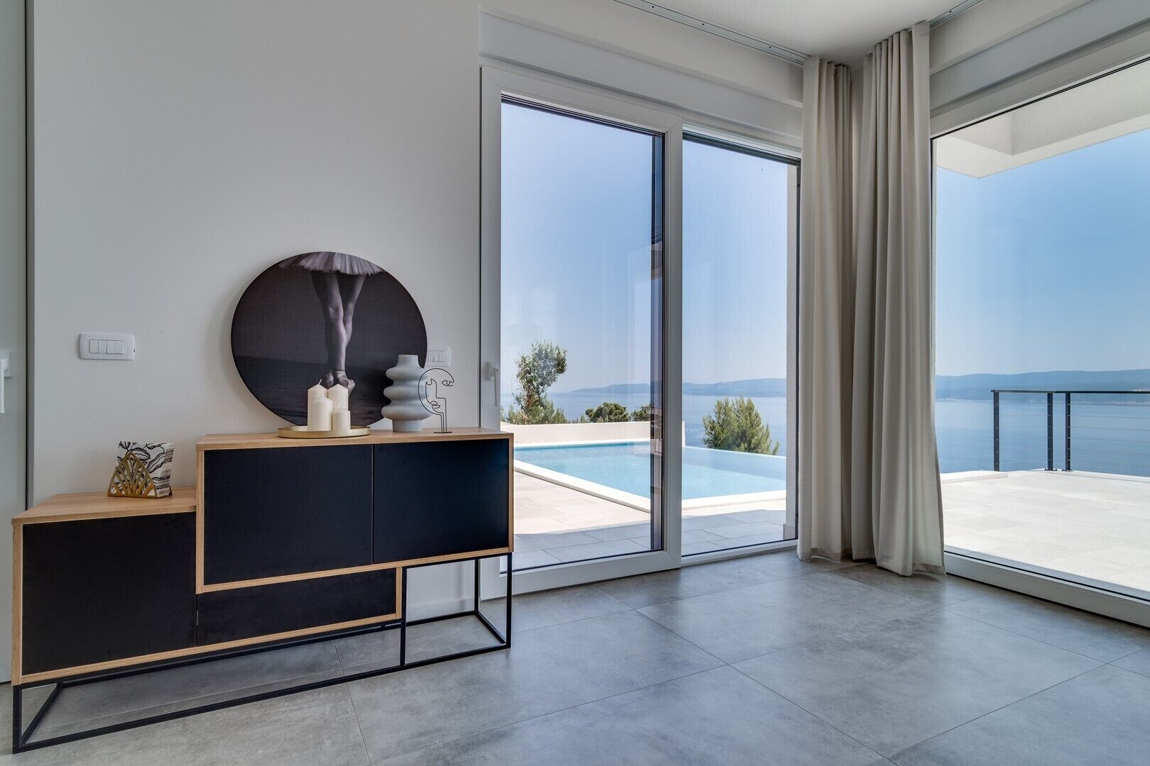 A modern room with a large sliding glass door leading to a balcony with a pool and a view of the sea.