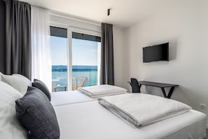 Une chambre d’hôtel avec deux lits, une télévision, un bureau et un balcon donnant sur la mer.