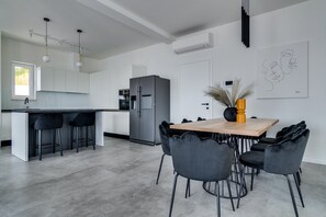 Una cocina moderna con una isla central, taburetes de bar, una mesa de comedor y sillas, y un refrigerador.