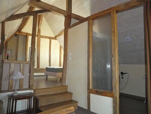 A room with a wooden staircase, a bed, a table with a lamp, and a large window.