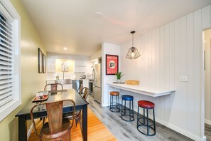 Une cuisine moderne avec des meubles blancs, un coin repas doté d’une table et de chaises en bois, et un bar avec des tabourets.