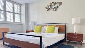 A modern bedroom with a wooden bed frame, a bedside table with a lamp, and a wall art piece above the bed.