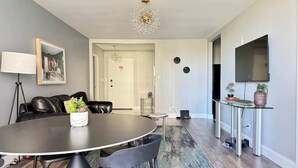 A modern living room with a round dining table, black leather sofa, and a chandelier.