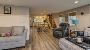 A spacious living area with a sofa, a chair, a coffee table, and a staircase leading to a kitchen. - Relax in Raymond's lakefront 2-bedroom vacation home, just steps to Sebago Lake (Raymond)