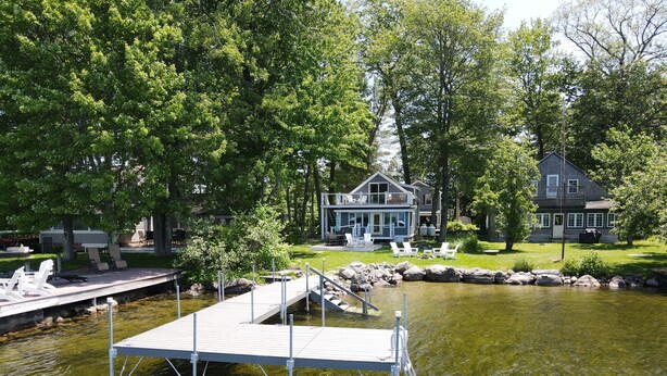 A lakeside property with a dock, outdoor seating, and a house in the background. - Relax in Raymond's lakefront 2-bedroom vacation home, just steps to Sebago Lake (Raymond)