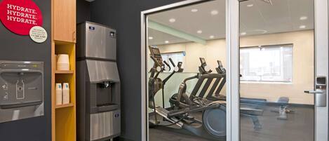 A modern fitness area with exercise equipment, a water dispenser, and a refrigerator.