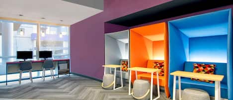 Un espacio de oficina moderno con una zona de recepción, asientos con cojines coloridos y un escritorio con dos monitores.