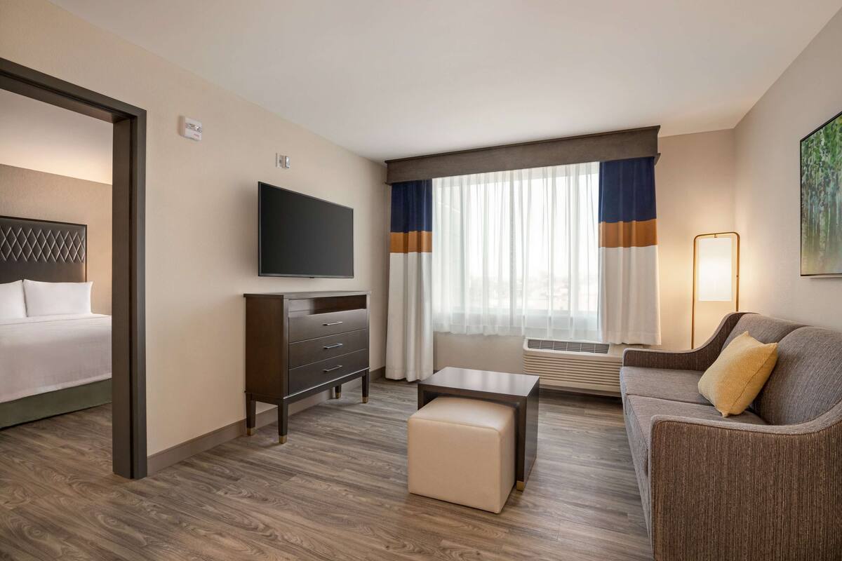 Une chambre d’hôtel avec un lit, une télévision, un bureau, un canapé et une fenêtre avec des rideaux.