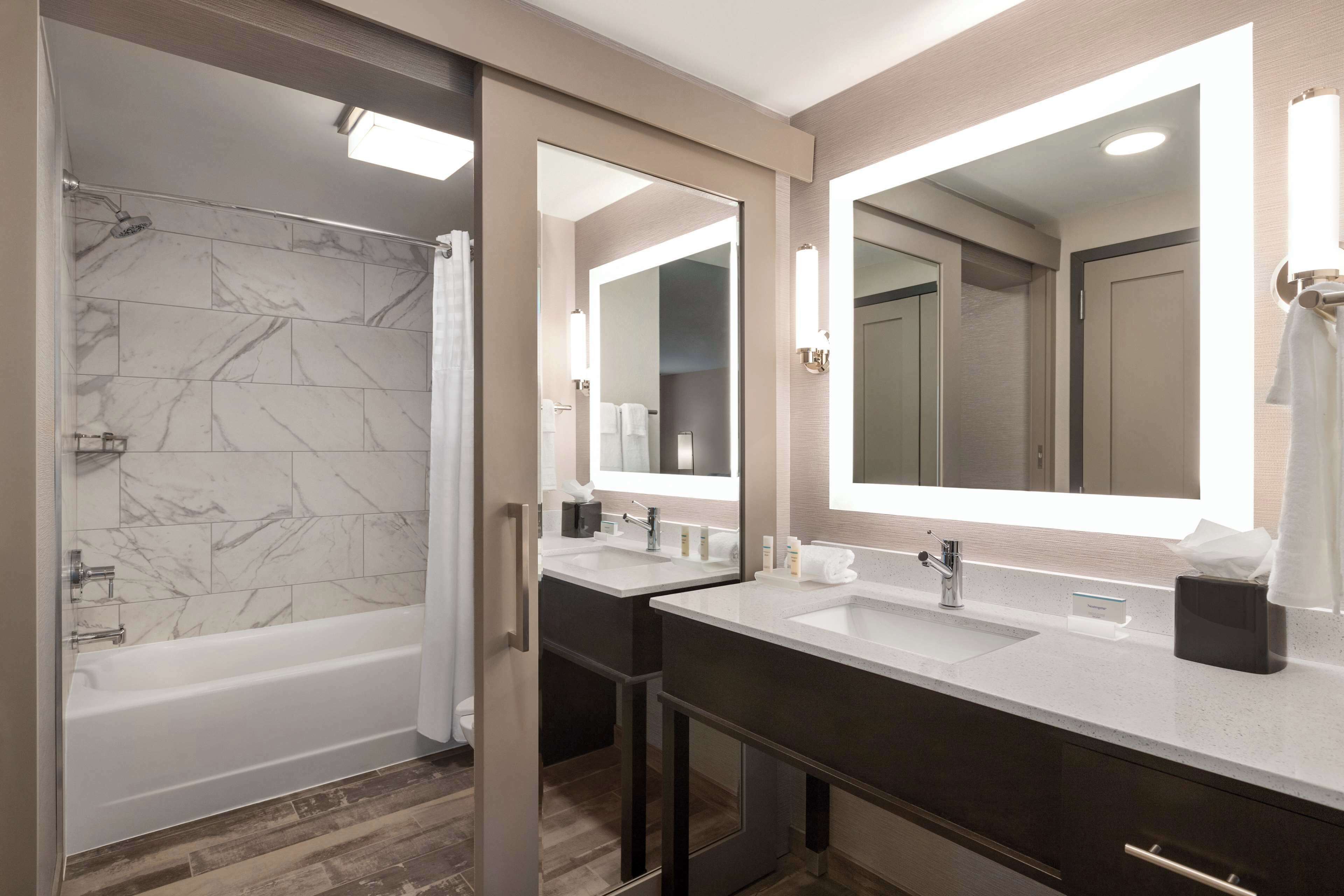 Un baño moderno con bañera, dos lavamanos y un espejo grande.