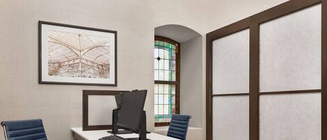 A conference room with a white table, two blue chairs, a computer, and a framed picture on the wall.