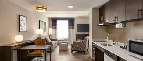 A modern hotel room with a kitchenette, a dining area, and a living space.
