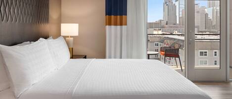 A hotel room with a large bed, a view of the city through a sliding door, and a cityscape visible through the window.