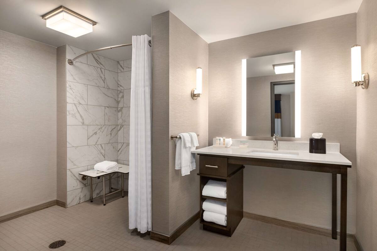 Une salle de bain moderne équipée d’une douche, d’un lavabo avec un miroir et d’un porte-serviettes.
